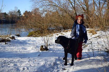 Siyah bir labradorla kışın yürüyüşe çıkan bir çocuk..