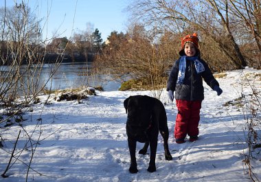 Siyah bir labradorla kışın yürüyüşe çıkan bir çocuk..