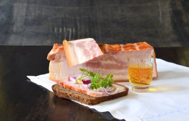 Bir parça göğüs eti, göğüs eti ve soğanlı sandviç ve beyaz peçetede bir kadeh viski..