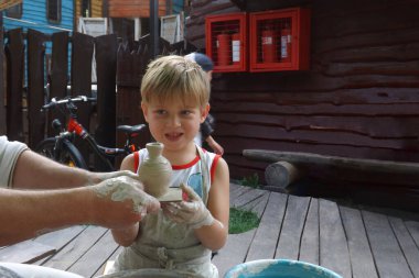 Çocuk, bir öğretmenin rehberliğinde çömlekçi çarkında bir gemi yaptı..