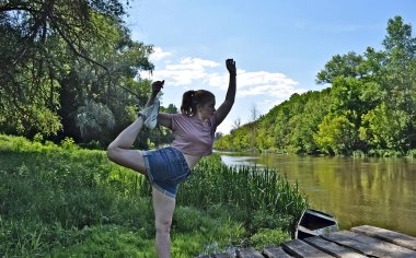 Genç bir kadın nehir kıyısında egzersiz yapıyor..