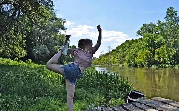 Genç bir kadın nehir kıyısında egzersiz yapıyor..