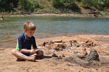 Yoğun bakışlı bir çocuk nehir kıyısında kale inşa eder..