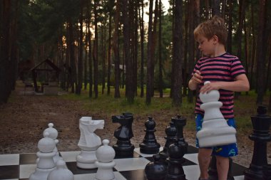 Bir çocuk akşamleyin parkta büyük bir satranç tahtasıyla satranç oynar..