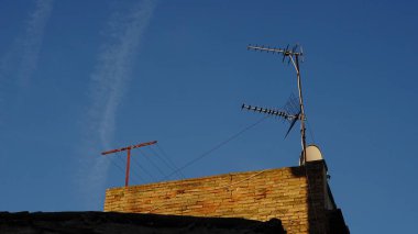 Gökyüzüne karşı antenleri ve çamaşır ipleri olan kır evinin çatısına.
