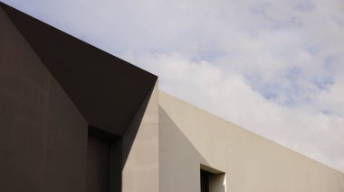 Bulutlu gökyüzüne karşı geometrik şekillerin ve pencerelerin modern cephesi