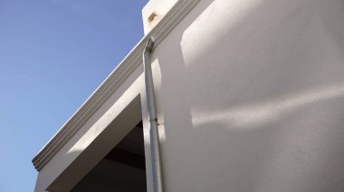 Gökyüzüne karşı beyaz cephede metalik yağmur suyu oluğu