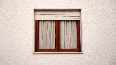 Panjurları ve beyaz perdeleri olan çift ahşap pencere.