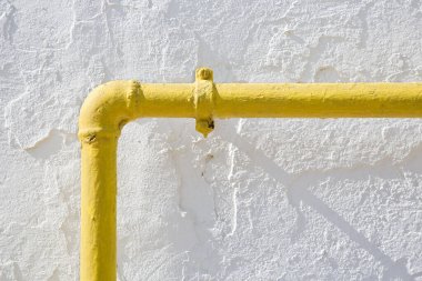 Methane gas and water yellow metal pipe against a white rough plaster wall 