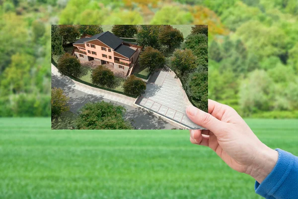 Land plot management - real estate concept with a vacant land on a green residential area available for building construction and hand holding a postcard about a project of a residential building