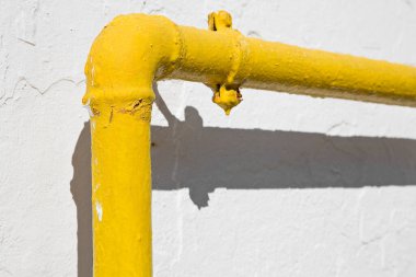 Methane gas and water yellow metal pipe against a white rough plaster wall 