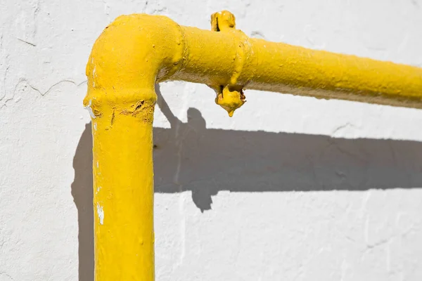 stock image Methane gas and water yellow metal pipe against a white rough plaster wall 