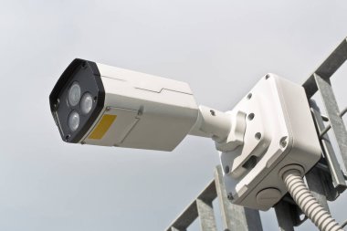 Security Camera against a metal grid for the security control of urban spaces clipart