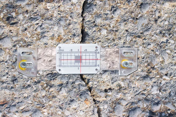 Deep crack in a damaged concrete wall cause due to subsidence of foundations structural failures with plastic mechanical crack meter designed to measure movement across surface cracks and joints