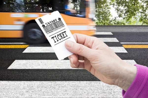 Hand holds a bus ticket - bus payment concept against a pedestrian crossing with bus that is coming