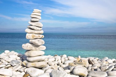 Mavi gökyüzüne ve sakin denize karşı yuvarlanan beyaz ve gri taşlar - sakin sahne ve fotokopi uzayı ile meditasyon konsepti