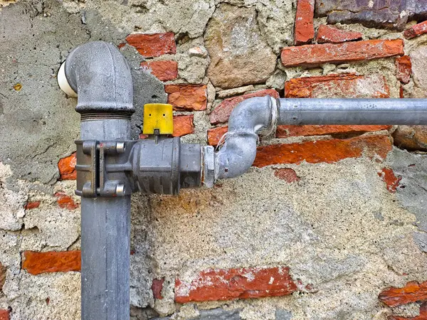Methane gas metal pipe with shut-off valve against a damaged brick wall