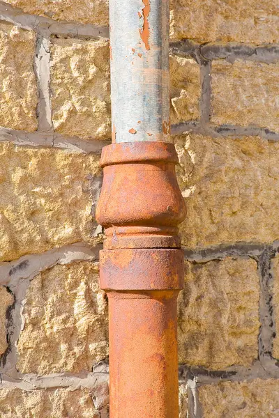 Old cast iron and copper downpipe against a stone wall
