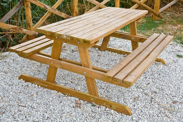 Yeni ahşap piknik masası beyaz çakıl zemini olan bir parkta.