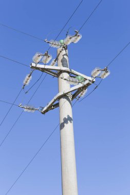 Beton elektrik direği, bakır elektrik kabloları ve cam yalıtıcılarıyla mavi arka planda.