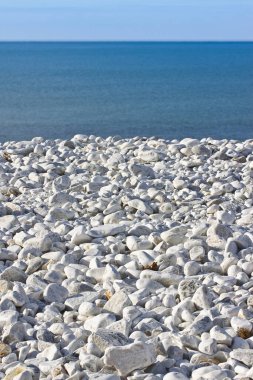 Beyaz ve gri taşları olan kumsal, mavi gökyüzüne karşı usulca yuvarlandı..