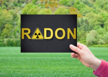 Tehlikeli Radon Gaz uyarısı - Konut inşaatı ve inşaat faaliyetleri için boş bir araziye karşı elinde kartpostal tutan kavram