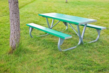 Galvanize metal borularda yeni boş piknik masası ve halka açık bir parkta yeşil bir çayırda yeşil plastik raflar.
