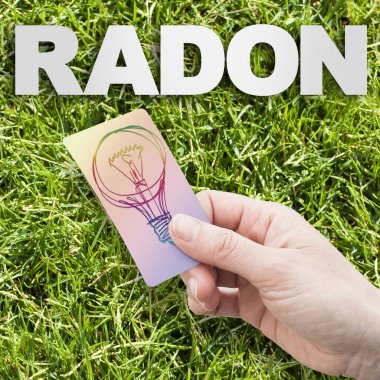 Radon çözeltisi konsept görüntüsü: Dünya 'dan gelen doğal radyoaktif gaz - yeşil biçilmiş çimlerin üzerinde radon yazılı konsept görüntü ve bir fikir lambası tutan el..