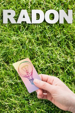 Radon çözeltisi konsept görüntüsü: Dünya 'dan gelen doğal radyoaktif gaz - yeşil biçilmiş çimlerin üzerinde radon yazılı konsept görüntü ve bir fikir lambası tutan el..