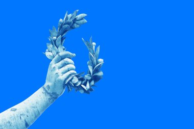 Hand holds a laurel wreath - bronze statue on colored background - Success and fame concept imag clipart