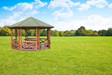 Wooden gazebos with picnic table and wooden bench in a green mowed lawn