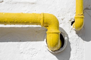 Methane gas and water yellow metal pipe against a white rough plaster wall 
