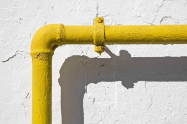 Methane gas and water yellow metal pipe against a white rough plaster wall 