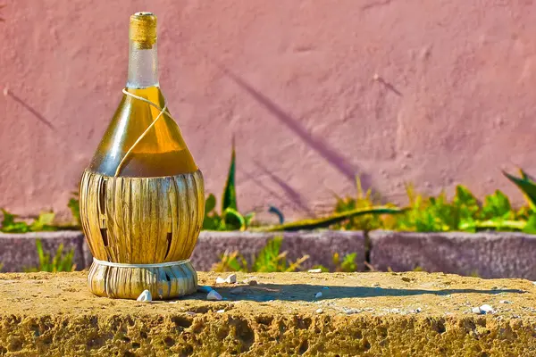 Tufa taş bloğunda saman kaplı şarap flama, kırsal bir duvara karşı dizilmiş.