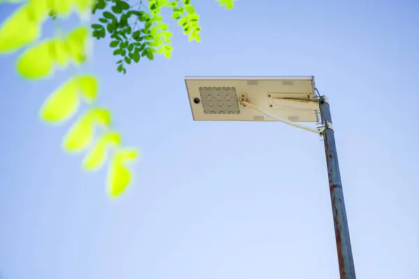 Public street lighting pole with LED lights with clear blue sky and green leaves foreground