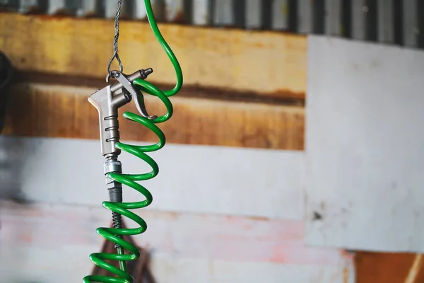 air gun with green spiral hose hanging on a metal hook in a workshop foreground focus. with copy space