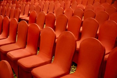 Kırmızı kaplamalı sıra sıra şölen sandalyeleri bir balo salonunda düzgünce düzenlenir.