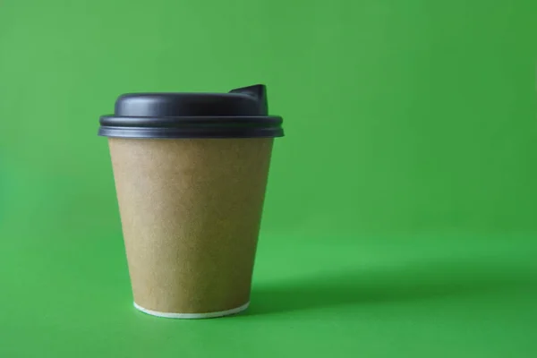 coffee to go in a disposable cup on a green background, you can place text, kraft paper cup. Takeaway paper coffee cup