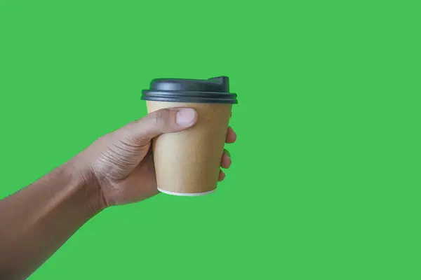 hand holding a Takeaway paper coffee cup. coffee to go in a disposable cup on a green background, you can place text or logo, kraft paper cup.