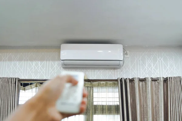 man's hand holding air conditioning unit remote control aimed at the AC unit. Man operating air conditioner with remote control indoors. adjusting the temperature. turn on or turn off the AC