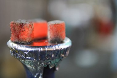 Nargile kömürü ve bulanık arka planlı shisha kasesi. Shisha için sıcak kırmızı kömür, arka planda bir nargile barında sobanın üzerinde ısındı. kopyalama alanı ile