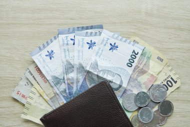 Cüzdanın altında rupiah banknotları var. Küçük bir değişiklik. Para bozdur. Para miktarı 1000 rupiah ve 2000 rupiah ve rupiah paralar üzerinde fotokopi alanı olan tahta bir masa.