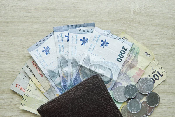 small denominations of rupiah banknotes under the wallet. small change. change money. money in the amount of 1000 rupiah and 2000 rupiah and rupiah coins with copy space on a wooden table