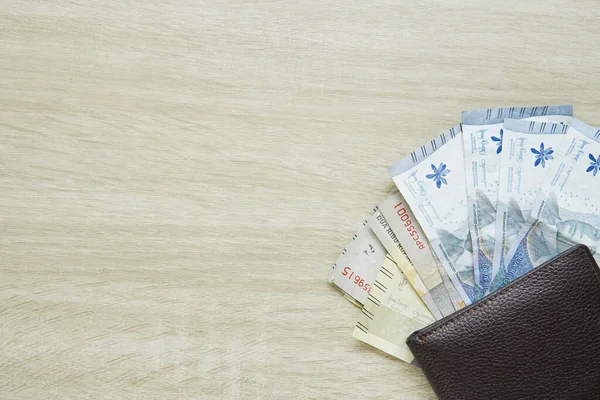 small denominations of rupiah banknotes under the wallet. small change. change money. money in the amount of 1000 rupiah and 2000 rupiah. with copy space on a wooden table
