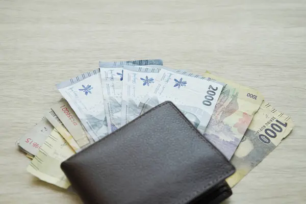 small denominations of rupiah banknotes under the wallet. small change. change money. money in the amount of 1000 rupiah and 2000 rupiah. with copy space on a wooden table