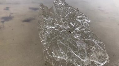 Kumlu sahilde şeffaf bir buz parçası.