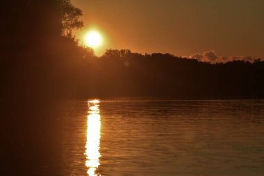 Gölün üzerinde altın gün batımı Ormanın üzerinde güneş diski