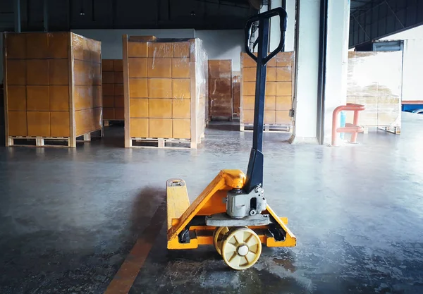 Hand Pallet Truck and Package Boxes Stacked on Pallets in Storage Warehouse. Forklift Loader. Cardboard Boxes, Parcels, Supplies Warehouse Shipping. Distribution Storehouse, Supply Shipment Boxes.