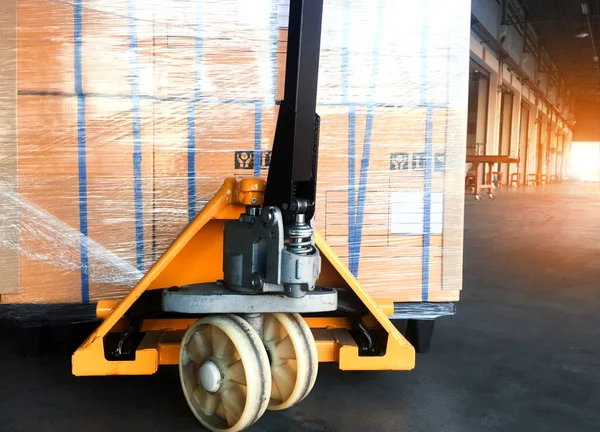 Hand Pallet Truck and Package Boxes Stacked on Pallets in Storage Warehouse. Forklift Loader. Cardboard Boxes, Parcels, Supplies Warehouse Shipping. Distribution Storehouse, Supply Shipment Boxes.