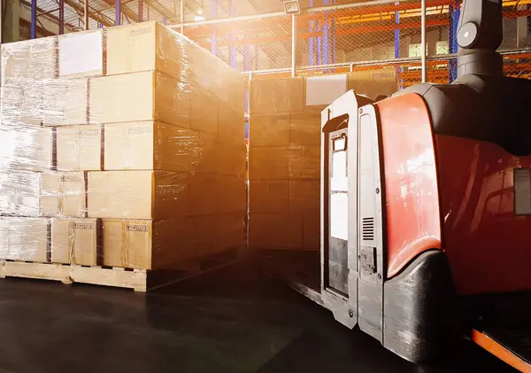 Forklift Pallet Jack and Package Boxes Stacked on Pallets in Storage Warehouse. Forklift Loader. Cardboard Boxes, Parcels, Supplies Warehouse Shipping. Distribution Storehouse, Supply Shipment Boxes.
